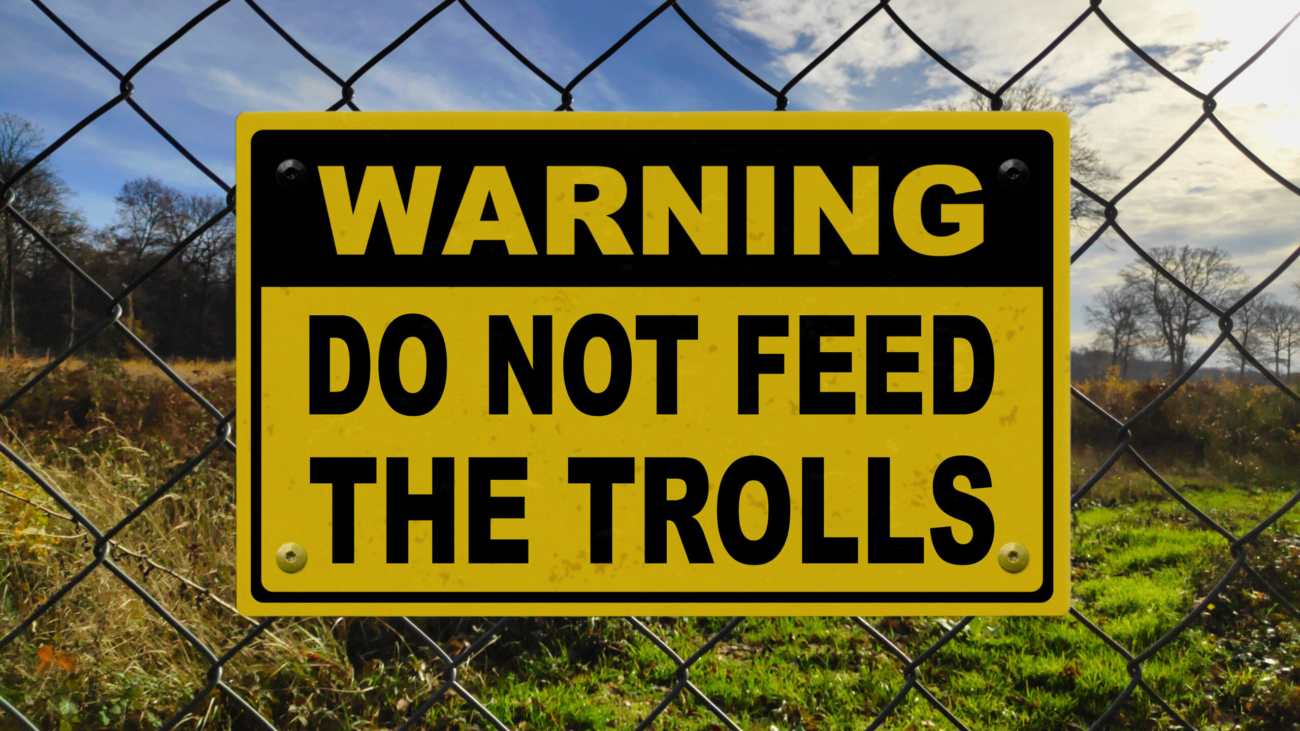 Black and yellow warning sign on a fence stating in "Warning - Do not feed the trolls".